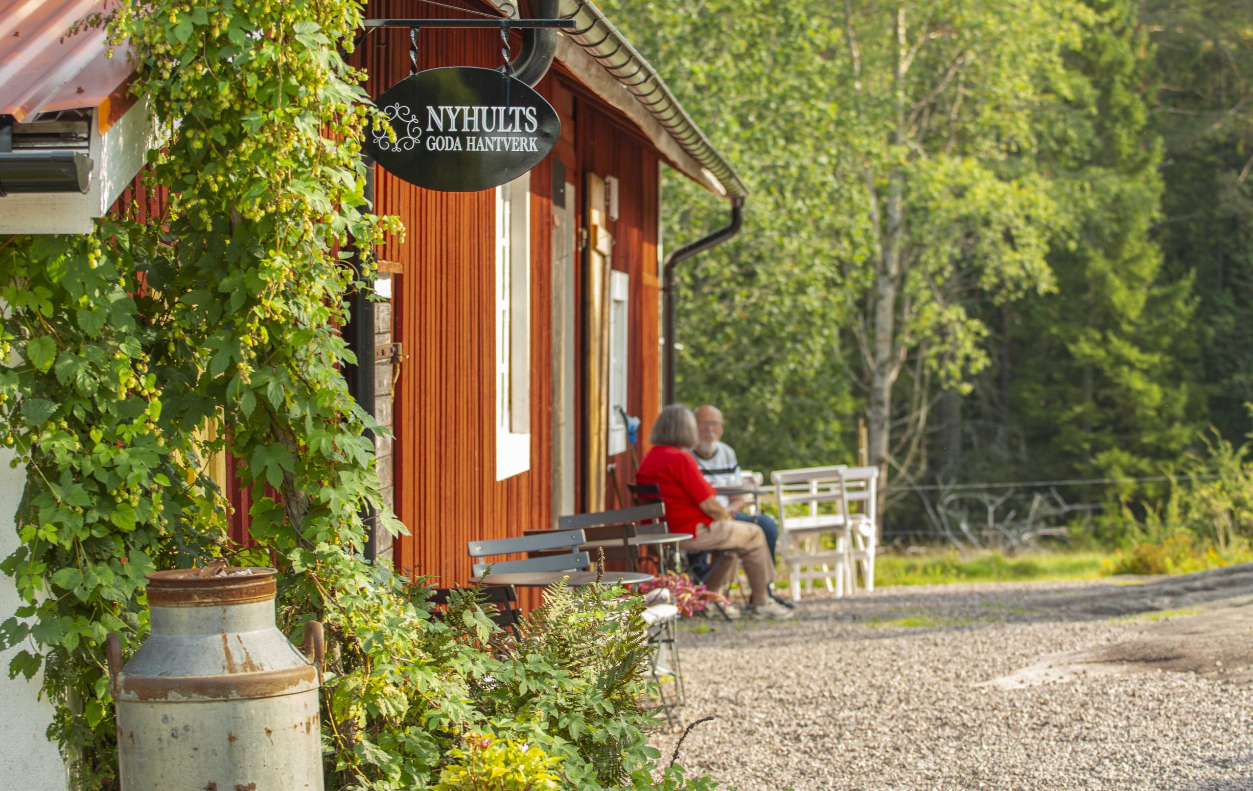Rött trähus med uteservering med grusad plan. Humle växer vid husknuten.